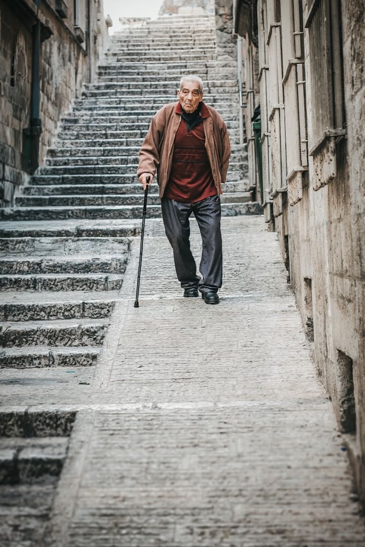 Elderly man with cane walks down stone stairs.