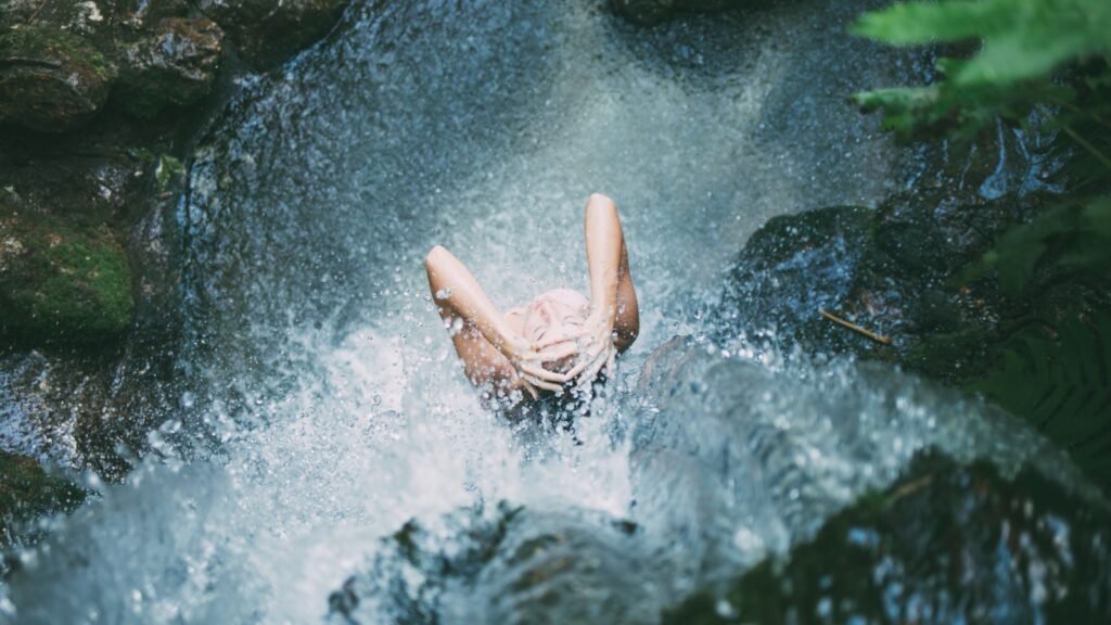 high-angle photography of woman bathing below waterfalls during daytime