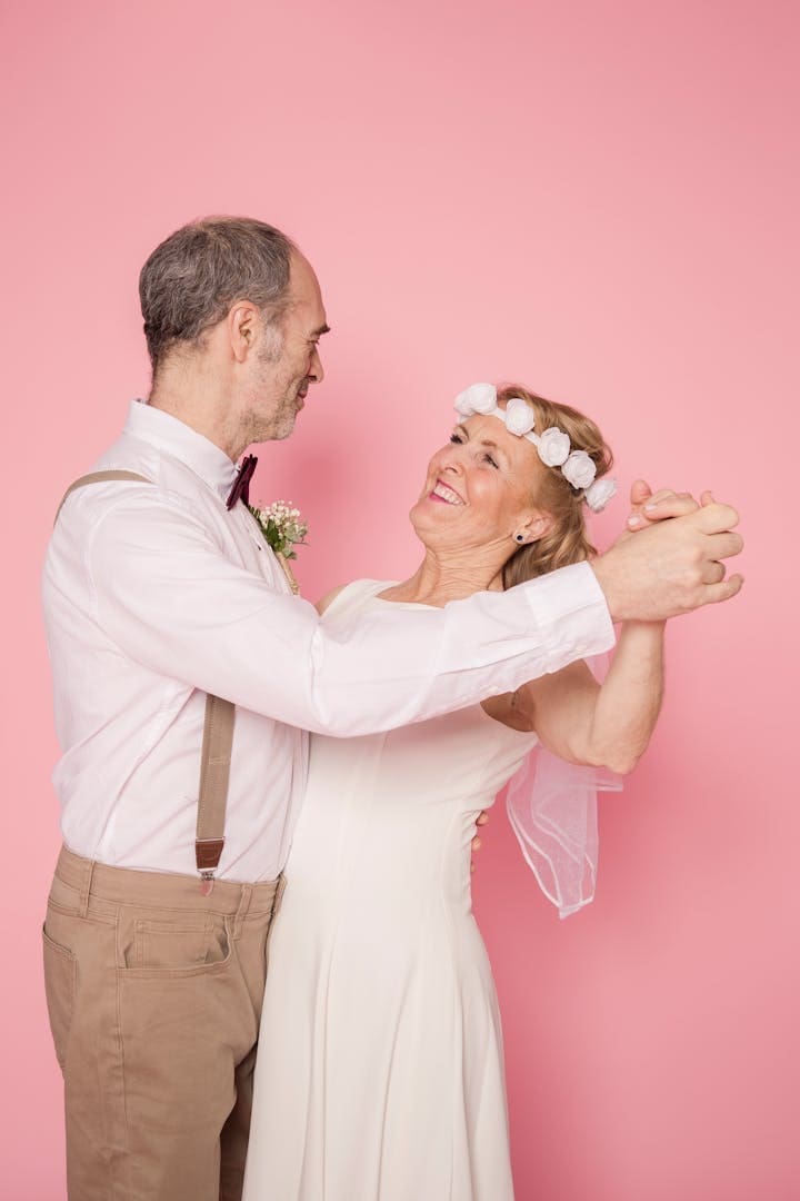 Charming elderly couple dancing joyfully against a pink backdrop.