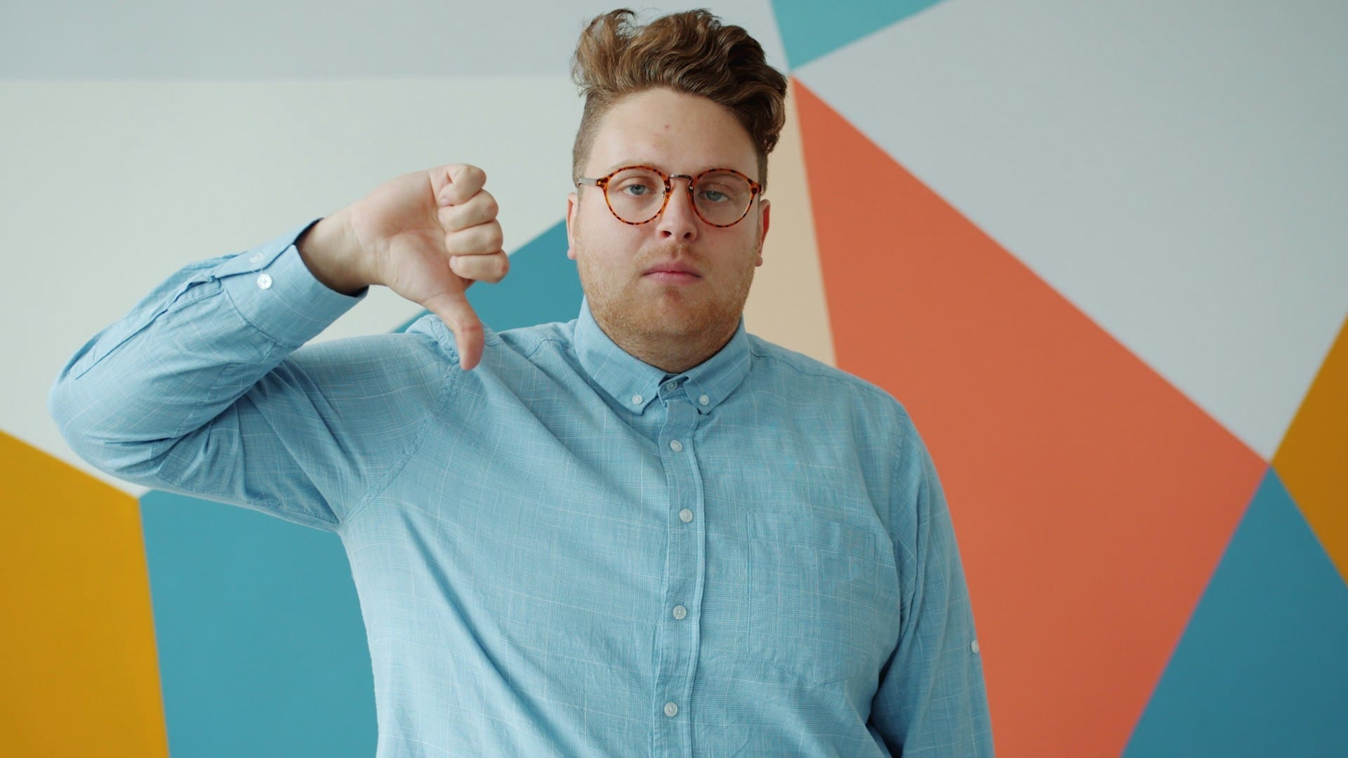 Man with glasses gives a thumbs down gesture.